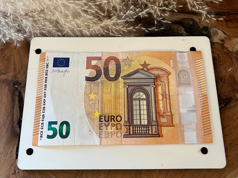 May include: A 50 euro bill with a building and stars on it. The bill is framed in a white frame with holes in the corners.