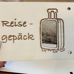 May include: A white wooden sign with the text "Reise-gep&auml;ck" and a cutout of a suitcase with a mirror inside.