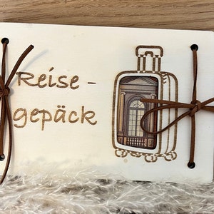 May include: A white wooden box with a brown leather strap and a cutout of a suitcase. The box has the text "Reise - Gep&auml;ck" written on it.