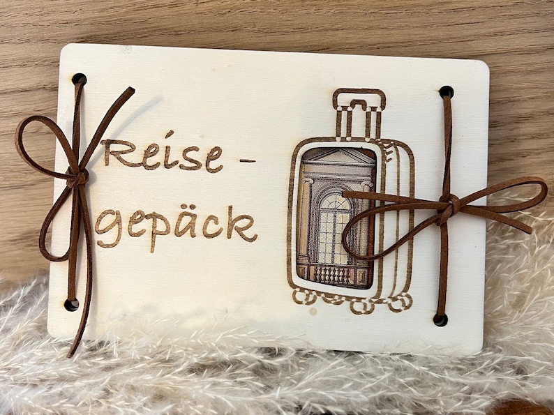 May include: A white wooden box with a brown leather strap and a cutout of a suitcase. The box has the text "Reise - Gep&auml;ck" written on it.