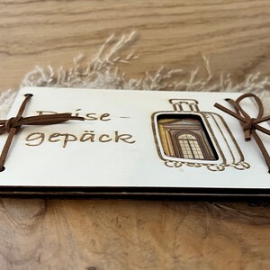 May include: White wooden box with a brown leather strap and the text "Reise-gep&auml;ck" on the front. The box has a cutout of a suitcase with a window.