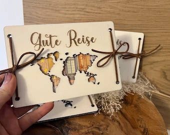 Könnte beinhalten: Ein weißes Holz-Reisetagebuch mit einem Ausschnitt einer Weltkarte und dem Text "Gute Reise" in brauner Schrift. Das Tagebuch ist mit braunem Lederband gebunden.