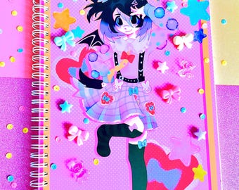 May include: A spiral-bound notebook with a pink cover featuring a colorful anime-style character illustration. The design includes stars, bows, and hearts. The notebook is decorated with various colorful embellishments.