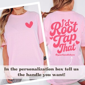 Puede incluir: Camiseta rosa claro con un coraz&oacute;n rojo en la parte delantera y la frase "I'd Root Tap That" en la parte trasera. El texto "@yourhandlehere" tambi&eacute;n est&aacute; en la parte trasera. La camiseta tiene mangas cortas.