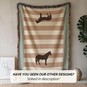 May include: A beige and brown striped throw blanket with a horse silhouette design. The blanket has a fringe border and a light green edge. The text "HAVE YOU SEEN OUR OTHER DESIGNS? *linked in description*" is at the bottom.