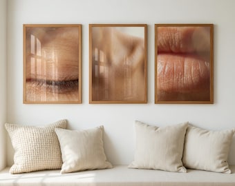 May include: Three framed art prints featuring close-up images of human skin: an eye, a shoulder, and lips. The prints are in wooden frames and hang on a white wall above a bench with pillows.