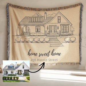 May include: A beige throw blanket featuring a black line drawing of a house, with the words "home sweet home" and the address "256 Harold Street" printed below. The blanket has a fringed edge and a photo of the house in the corner.