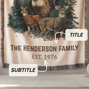 May include: Beige woven throw blanket with a forest scene and deer, and the text "THE HENDERSON FAMILY EST. 1976". The blanket has a fringed edge and a detailed illustration of deer.