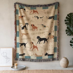 May include: A woven throw blanket featuring a repeating pattern of various dog breeds in brown, black, and tan. The blanket has a beige background with green and blue border and fringe.