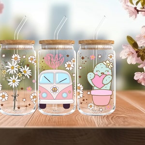 Könnte beinhalten: Drei Glasbehälter mit Bambusdeckeln und Strohhalmen. Jeder Behälter hat ein anderes Design: ein Strauß Gänseblümchen, ein rosa Van mit den Worten "Stay groovy" und ein Kaktus, der ein Herz hält.