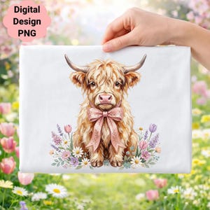 May include: A white rectangular item featuring a watercolor illustration of a Highland cow with a pink bow, surrounded by flowers. The text "Digital Design PNG" is in the upper left corner. The item is held by a hand.