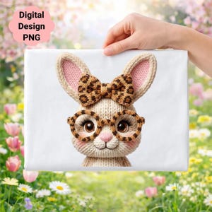 Puede incluir: Un lienzo blanco con un diseño de conejito tejido. El conejito tiene una pajarita y gafas con estampado de leopardo, orejas internas rosas y lleva gafas. El texto "Digital Design PNG" está en forma de nube rosa.