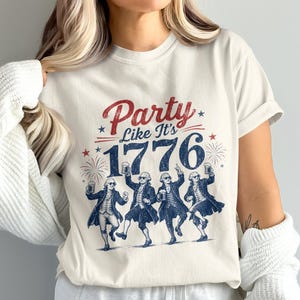 White t-shirt with "Party Like It's 1776" and graphic of dancing founding fathers holding beers.
