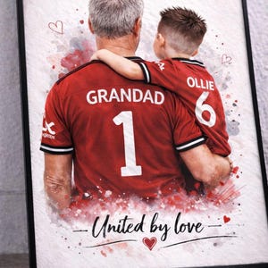 May include: Framed art print featuring a watercolor style image of a grandfather and grandchild in matching red jerseys. The jerseys display "GRANDAD 1" and "OLLIE 6". The text "United by love" is written below.