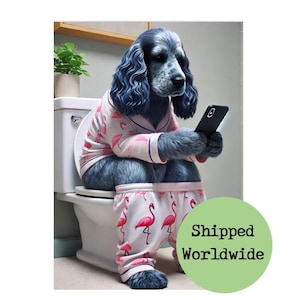 May include: A blue dog wearing pink flamingo pajamas sits on a toilet while holding a smartphone. The pajamas have a pink and white pattern. A small plant sits on the toilet tank.