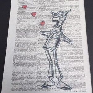 Pu&ograve; includere: Un'illustrazione in bianco e nero dell'Omino di Latta del Mago di Oz, disegnata su una pagina di dizionario vintage. La pagina presenta la parola "Wombat" e la parola "Wood". Tre cuori rossi sono disegnati intorno all'Omino di Latta.