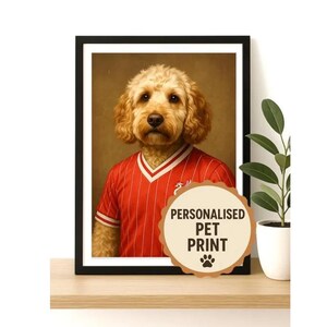 Może przedstawiać: Oprawiony portret zwierzaka z golden doodle w czerwono-białej koszulce w paski. Nadruk zawiera okrągły emblemat z napisem "PERSONALISED PET PRINT" i odciskiem łapy. Grafika jest wyświetlana na drewnianej półce.