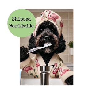 Peut inclure: Un chien noir portant une robe blanche à imprimé flamant rose et une serviette blanche sur la tête se brosse les dents avec une brosse à dents. Le chien est dans une salle de bain avec un lavabo blanc et un distributeur de savon argenté.