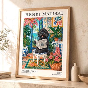 Pode incluir: Uma impressão de arte emoldurada intitulada HENRI MATISSE com um cão preto de pelo encaracolado sentado num banco branco a ler um jornal. A cena retrata um interior colorido com plantas em vasos, azulejos azuis e brancos e vista para o mar.