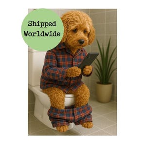 May include: A brown and white dog wearing a red and blue checked shirt and trousers sits on a white toilet seat. The dog is holding a black smartphone in its paws. The dog is looking at the phone. The text "Shipped Worldwide" is in a green circle in the top left corner of the image.