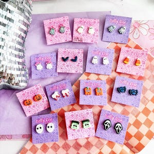 May include: A collection of Halloween-themed stud earrings on branded Nelly Rose Jewelry cards. Designs include ghosts, pumpkins, candy corn, bats, teeth, spiders, mummies, Frankenstein monsters, and ghost-face masks in various colors.