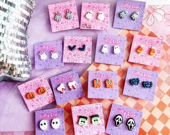 Könnte beinhalten: Eine Sammlung von Halloween-Ohrsteckern auf gebrandeten Nelly Rose Jewelry-Karten. Die Motive umfassen Geister, Kürbisse, Zuckermais, Fledermäuse, Zähne, Spinnen, Mumien, Frankenstein-Monster und Geistermasken in verschiedenen Farben.