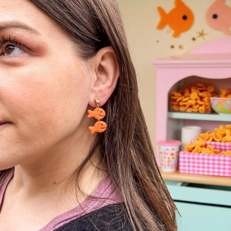 A woman wearing orange fish-shaped earrings is shown in the image.