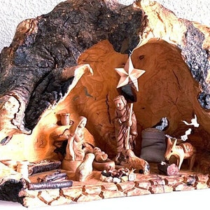 May include: A carved wooden nativity scene depicting the holy family, animals, and a star. The figures are set within a rustic, natural wood structure. The scene includes a star, a donkey, and a baby in a manger.
