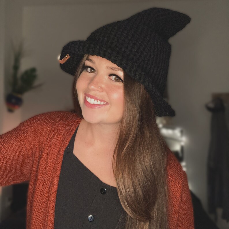 May include: A black crochet witch hat with a pointed crown and a wide brim. The hat has a textured appearance and a small leather tag. This handmade hat is perfect for Halloween or costume parties.
