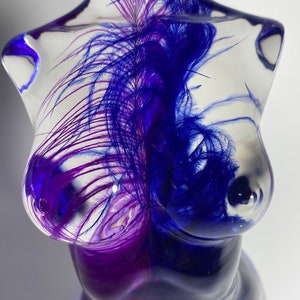 May include: A clear glass sculpture of a torso with purple and blue feathers embedded inside. The feathers are arranged in a swirling pattern.