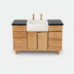 May include: A miniature wooden bathroom vanity with a white sink, gold taps, and black countertops. The vanity has multiple drawers and cabinet doors, and is set on short, rounded legs. A charming piece for a dollhouse or miniature collection.
