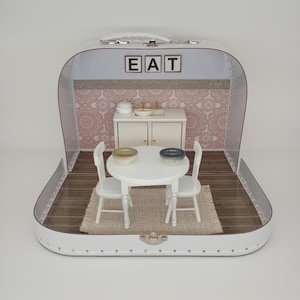 May include: A miniature kitchen scene inside a white suitcase. The scene includes a small white table and two chairs, a rug, a cabinet, and a sink. The word "EAT" is displayed above the cabinet. The background features a pink floral pattern.