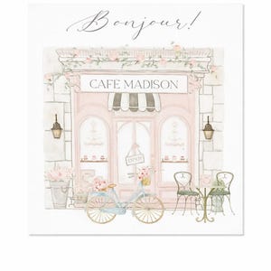 May include: Watercolor illustration of a pink cafe with the text "Cafe Madison" and "Bonjour!". A light blue bicycle with a basket of flowers is parked in front. Two chairs and a small table are set up outside.