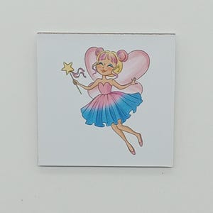 May include: A square illustration of a fairy with pink and blue attire. The fairy has blonde hair, pink wings, and is holding a gold star wand. The fairy is smiling and appears to be floating.