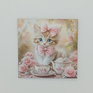 Pode incluir: Impressão em tela quadrada com um gatinho de olhos azuis, usando um laço e coleira rosa. Um conjunto de chá com rosas cor-de-rosa é disposto ao redor do gatinho. O fundo é um design floral suave e desfocado.