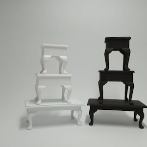 May include: Three miniature tables stacked on top of each other. The top two tables are white and the bottom table is black.