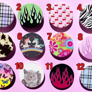 May include: Twelve different phone pop socket designs. The designs include plaid, flames, cherries, zebra print, cow print, unicorns, flowers, a kitten, and butterflies.