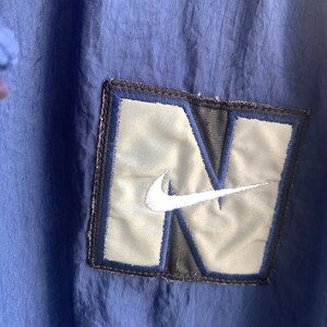 May include: A navy blue jacket with a large, silver and black embroidered patch featuring the Nike swoosh logo.