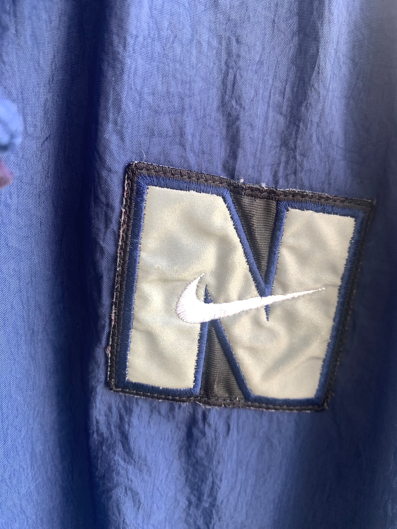 May include: A navy blue jacket with a large, silver and black embroidered patch featuring the Nike swoosh logo.