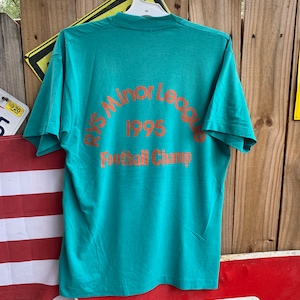 May include: A teal blue t-shirt with an orange circle graphic that says "PYS Minor League 1995 Football Champ".