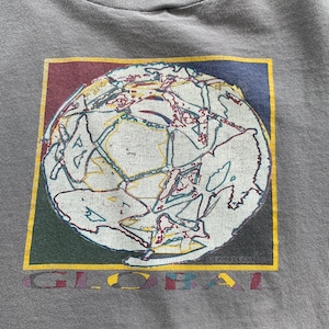 May include: A grey t-shirt featuring a graphic of a globe within a colourful square frame. The globe is white with colourful lines and the text "GLOBAL" is printed below the graphic.