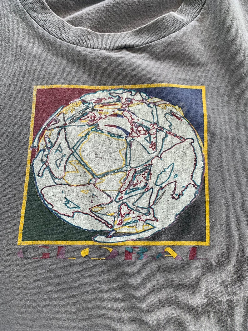 May include: A grey t-shirt featuring a graphic of a globe within a colourful square frame. The globe is white with colourful lines and the text "GLOBAL" is printed below the graphic.