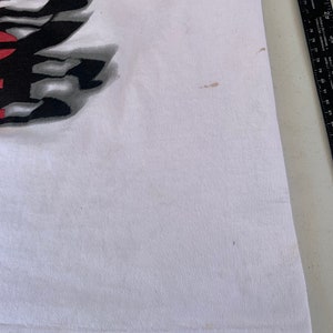 May include: White t-shirt with a black and white graphic print. The print features a stylized design with the word "Revolution" in bold letters.