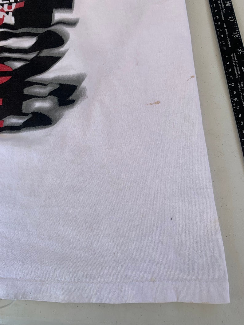 May include: White t-shirt with a black and white graphic print. The print features a stylized design with the word "Revolution" in bold letters.