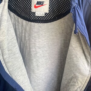 May include: A navy blue jacket with a black mesh lining and a white Nike logo tag. The tag says "Nike" and "L G G" and "Made in Malaysia".