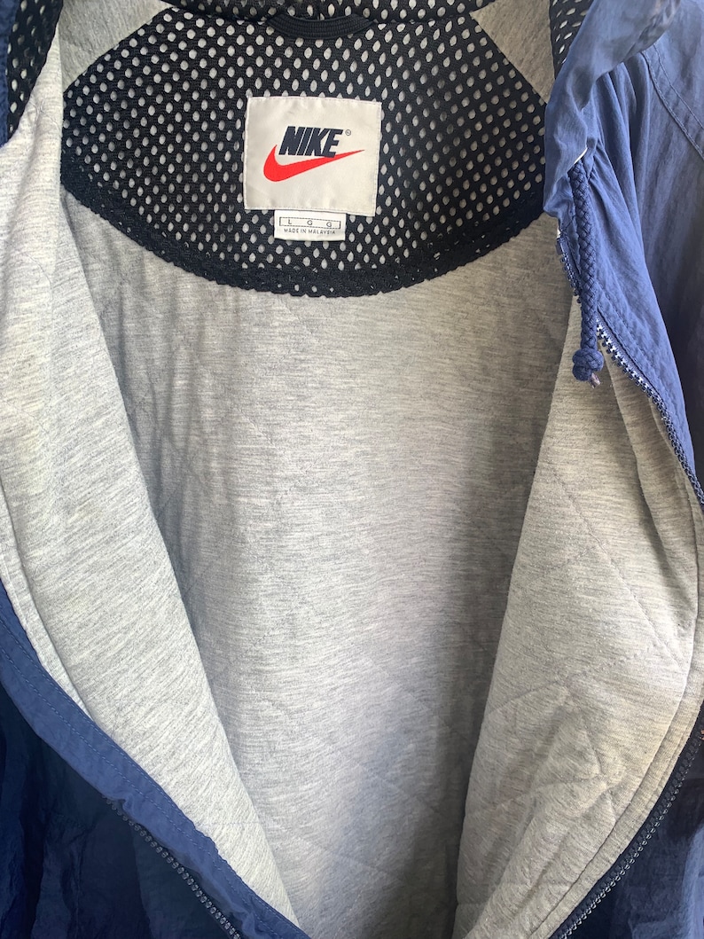 May include: A navy blue jacket with a black mesh lining and a white Nike logo tag. The tag says "Nike" and "L G G" and "Made in Malaysia".