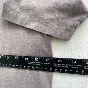 May include: A close-up of a grey fabric with a ruler measuring 59 centimetres. The ruler has black markings and the text "LINS AR METRIC UNITS AND SYMBOLS 1000 millimetres (mm) = 1 metre (m)" printed on it.