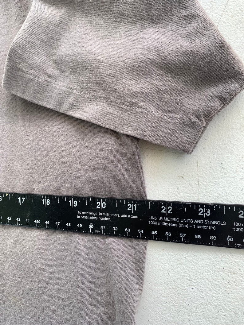 May include: A close-up of a grey fabric with a ruler measuring 59 centimetres. The ruler has black markings and the text "LINS AR METRIC UNITS AND SYMBOLS 1000 millimetres (mm) = 1 metre (m)" printed on it.