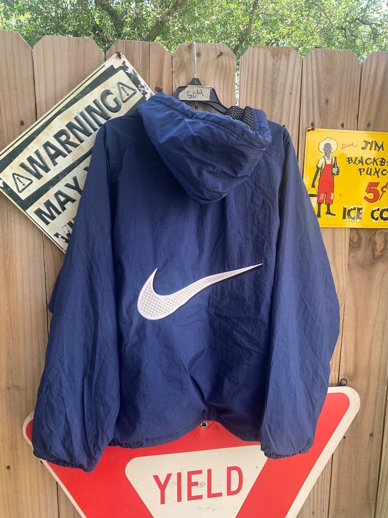 May include: A navy blue hooded jacket with a white Nike swoosh logo on the back. The jacket has a zip fastening and a mesh lining.