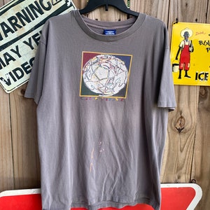 May include: A grey t-shirt featuring a graphic of a colourful globe with the word "Global" printed beneath it. The shirt has a crew neck and short sleeves. The brand name "Umbro" is printed on the tag.